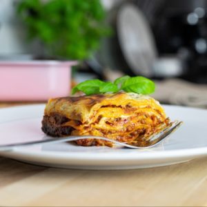 une belle portion de lasagne est sur petite assiette avec un basilic dessus